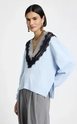 Sweater de punto color celeste con escote en V profundo, ribete acanalado gris y aplicación de encaje negro que delinea el escote. Presenta mangas largas con puños acanalados y dobladillo acanalado.