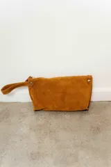 Sobre de mano tipo clutch confeccionado en cuero agamuzado color tostado, con cierre superior y correa de muñeca integrada.