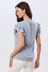 Camisa de lino y viscosa color beige, con cuello mao, escote en V y botones frontales de madera. Presenta mangas cortas con volados delicados.