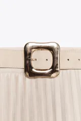 Falda midi plisada de tiro alto color beige, con cinturón a tono y hebilla metálica dorada. Cierre lateral con cremallera oculta.