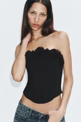 Top corsetero negro de escote recto y hombros descubiertos, con varillas interiores y detalle de aplicaciones de flores de tela en el borde superior. Cuenta con cierre lateral con cremallera oculta.