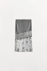 Falda midi de tiro medio, color gris, confeccionada en mezcla de lyocell y viscosa, con detalle de apliques de lentejuelas y bajo de tejido transparente plisado con bordados florales.