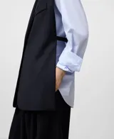 Chaleco sastrero sin mangas, color azul marino, con solapas de traje, cierre frontal de botón oculto y bolsillos de vivo en el pecho y la cadera. Presenta aberturas laterales y espalda corta.