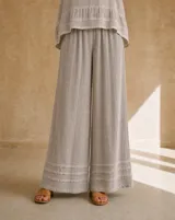 Pantalón beige de corte amplio y fluido, con cintura elástica fruncida y detalles de costuras horizontales en los bajos.