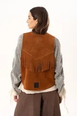 Chaleco oversize confeccionado en cuero descarne, con diseño de terminación en picos, detalle de tachas metálicas en los bordes frontales y flecos en la espalda.