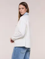 Campera de denim blanco de corte holgado con hombros caídos, cuello con solapa en contraste de color celeste, cierre frontal con botones metálicos y bolsillos delanteros con solapa.