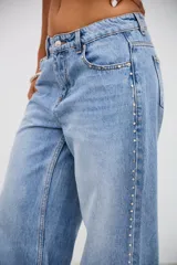 Jean de tiro medio en color celeste, con corte recto y holgado. Presenta detalle de tachas metálicas pequeñas a lo largo de las costuras laterales y en la zona de los bolsillos delanteros.