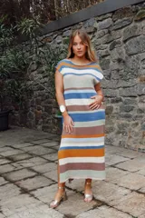 Vestido largo de tejido de punto, con rayas horizontales en tonos tierra, azul y blanco. Presenta cuello redondo, mangas cortas caídas y aberturas laterales en el ruedo.