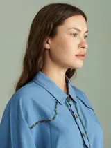 Camisa de algodón color azul con cuello clásico y cierre frontal de botones. Presenta detalles de vivos en estampado cuadrillé en la solapa, el canesú y los puños.