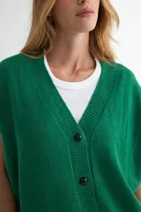 Chaleco de punto color verde, con escote en V y cierre frontal de botones negros. Presenta un diseño holgado con terminaciones acanaladas en el cuello, sisas y ruedo.