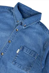 Camisa de jean celeste oscuro, de corte clásico, con cuello abotonado, manga larga y bolsillo en el pecho.