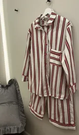 Conjunto de pijama de dos piezas compuesto por una camisa de manga larga con botones frontales y un pantalón de corte holgado, ambos con estampado de rayas verticales en tonos azul y blanco. El pantalón cuenta con un detalle de vivo en color oscuro en el ruedo.