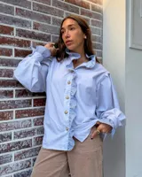Camisa de manga larga abullonada en color rosa con rayas verticales finas. Presenta un diseño con volados en el cuello y a lo largo de la botonadura frontal, puños con detalle de rayas contrastantes y botones decorativos dorados.