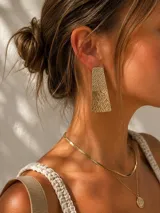 Aros colgantes dorados de forma trapezoidal con textura martillada y acabado brillante.
