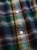 Camisa de manga larga confeccionada en tela de franela con estampado de cuadros en tonos azul claro, blanco y negro. Presenta cuello clásico, cierre frontal con botones y un bolsillo en el pecho.