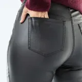 Pantalón de cuero sintético negro de corte recto, con cierre frontal de botones a la vista y tiro alto.