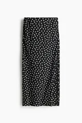 Pollera midi negra con estampado de lunares blancos, tiro alto, cintura elástica con fruncidos laterales y abertura pronunciada en un lateral.