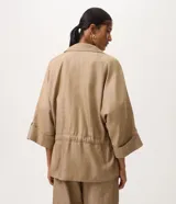 Campera tipo parka de la marca Marfinno, confeccionada en mezcla de algodón, viscosa y lino en color beige. Presenta cuello camisero, cierre frontal con botones, bolsillos con solapa en el pecho y cintura ajustable con cordón y lazo. Las mangas son largas con puños abotonados.