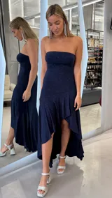 Vestido largo azul marino con acabado brillante, diseño strapless y corte asimétrico con volados en la falda.