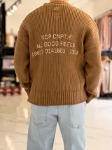 Sweater de punto color marrón, de manga larga, con textura acanalada y texto bordado en la espalda.