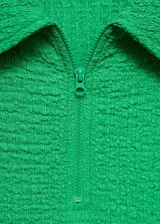 Vestido corto de color verde vibrante con textura arrugada. Presenta cuello polo, cierre frontal con cremallera y mangas cortas con terminación ondulada. Diseño entallado al cuerpo.