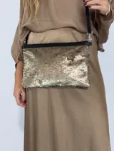 Cartera tipo sobre con lentejuelas doradas y negras reversibles, con borde superior de cuero negro y correa fina de cuero negro.