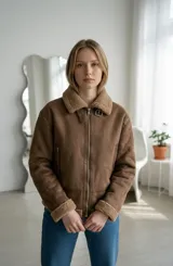 Campera tipo aviador de gamuza color camel, con interior y cuello de corderito sintético. Presenta cierre frontal metálico, bolsillos laterales con cierre y puños con detalle de corderito.