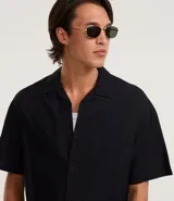 Camisa de manga corta color negro, con diseño boxy, cuello clásico y abotonado frontal.