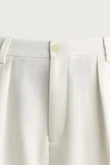 Pantalón relaxed fit de color blanco off-white, confeccionado en tejido con lino. Cuenta con pliegues frontales en la cintura, bolsillos delanteros y cierre frontal con cremallera y botón.