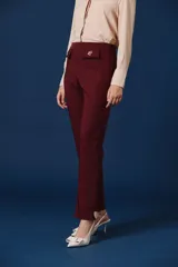 Pantalon de vestir color verde oscuro, de corte recto y tiro alto. Presenta dos solapas decorativas en la cintura con apliques de broches metálicos con forma de insectos.