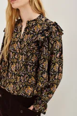 Camisa de manga larga con estampado paisley en tonos negros, amarillos y rosados. Presenta volados en los hombros, puños con terminación en volado y cierre frontal con botones.