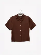 Camisa manga corta color marrón confeccionada en una mezcla de lino y tencel, con cuello camisero y cierre abotonado al frente.