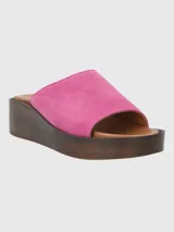 Sandalia tipo mule con plataforma de madera oscura y capellada de gamuza en color fucsia.