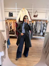 Trench de ecocuero negro con diseño cruzado de doble abotonadura, solapas clásicas, puños ajustables y largo midi.