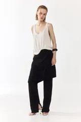 Pantalón recto de color negro con pollera mini superpuesta de corte asimétrico y cierre oculto lateral.
