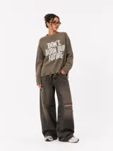 Sweater de punto color gris con efecto desgastado, cuello redondo, mangas largas y detalle de ruedo desflecado. Presenta una estampa frontal con la frase 'Don't burn our future' en color blanco.