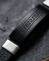 Pulsera masculina con banda central de cuerina negra grabada con diseño de guarda griega y detalles laterales en acero inoxidable.