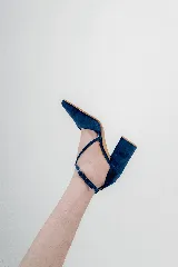 Zapato de taco alto azul oscuro, confeccionado en gamuza, con diseño de punta fina, escote en V y tiras cruzadas en diagonal con hebilla ajustable en el tobillo.