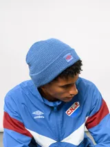 Gorro tipo beanie de tejido de punto acanalado en color azul, con parche frontal que incluye el logo de Umbro y la inscripción Nacional.