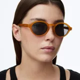 Lentes de sol con montura redonda de estilo retro en color ámbar y lentes polarizadas oscuras. Fabricados con materiales bio-based y propionato de celulosa, cuentan con protección UV400 y recubrimiento resistente a rayones.