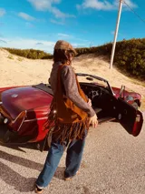 Bolso marrón de gamuza con flecos largos, asa de hombro y detalle de pasamanería con nudos.