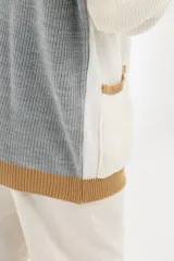 Cárdigan tejido de punto grueso, con diseño color block en gris, blanco y beige. Tiene cuello en V, cierre frontal con botones y un bolsillo de parche.