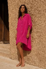 Vestido camisero corto de lino color naranja, con mangas largas arremangables mediante tira con botón, cierre frontal con botones y diseño amplio de corte asimétrico con la parte trasera más larga.
