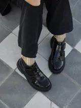 Borcego de cuero color marrón oscuro con acabado desgastado en la puntera. Presenta un diseño de caña corta con cierre lateral y dos tiras ajustables con velcro en el empeine. Cuenta con una suela de goma robusta tipo tractor.