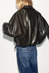 Chaqueta estilo bomber de efecto piel en color marrón oscuro, con cuello solapa, cierre frontal con cremallera, bolsillos delanteros de vivo y bajo acabado en elástico.