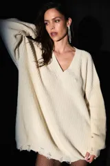 Sweater oversized color crema, tejido de punto con escote en V, roturas en ruedo y puños, y badana de PU en la espalda.