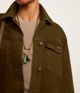 Campera trucker color verde oliva confeccionada en sarga de algodón, con cuello inglés, manga larga, bolsillos delanteros con solapa y abotonado delantero.