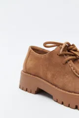 Zapato de gamuza color marrón con cordones, puntera con costura marcada y suela robusta dentada.