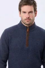 Buzo tejido de punto grueso en color azul marino, con cuello alto y cierre frontal parcial. Presenta detalles en gamuza en la zona del cierre y una textura en relieve en toda la prenda.