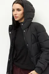 Campera puffer color tostado con capucha, cierre frontal con botones a presión y bolsillos laterales. Presenta diseño acolchado, puños elásticos y ajuste en la cintura.